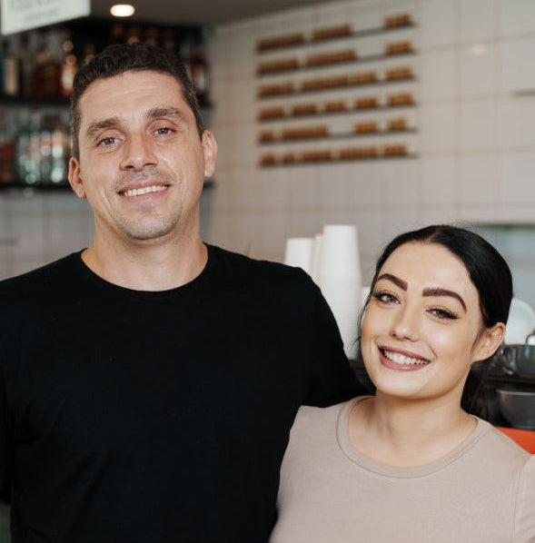 Two adults standing together in a casual setting, possibly a cafe or restaurant.