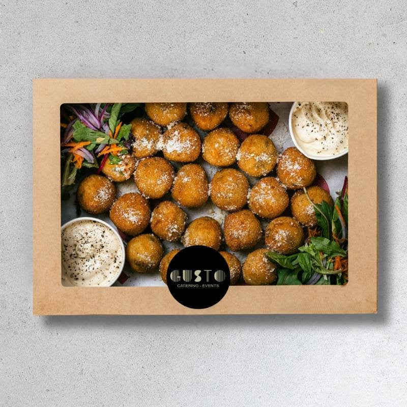 Box of fried balls with dipping sauces and salad on a gray background