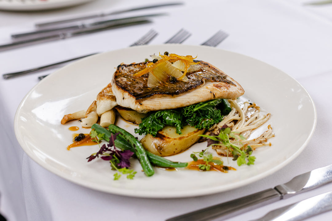 Plated dish with grilled fish, vegetables, and noodles on a white plate.