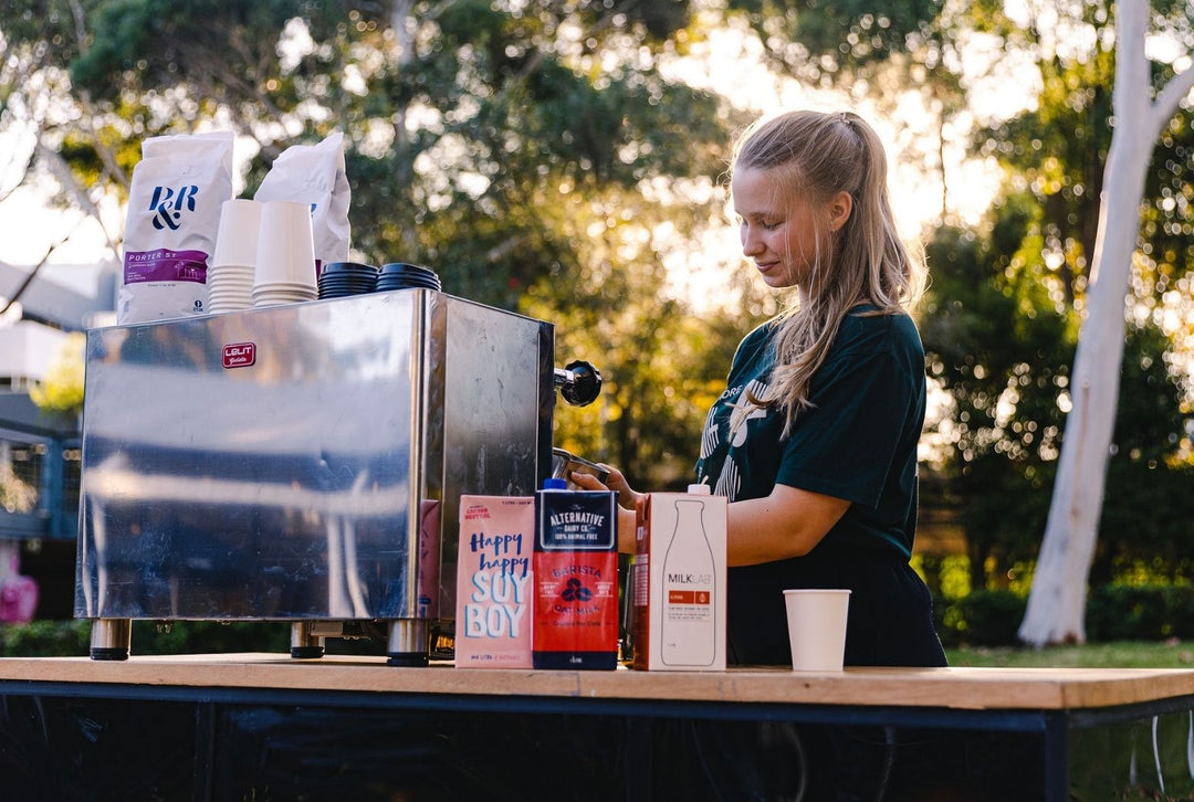 Woman preparing coffee at an outdoor event with a coffee machine and coffee bags.