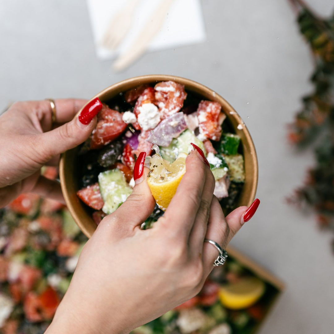 Person holding a bowl of salad with a lemon wedge, blurred background