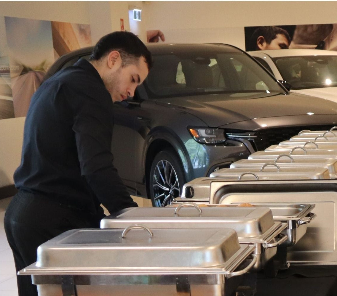 Person organizing metal trays in a car dealership with cars and promotional materials in the background