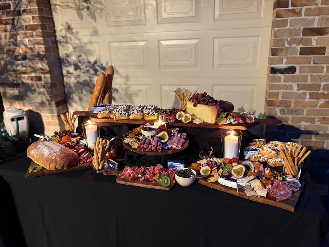 Assorted food platter with meats, cheeses, and bread on a table against a brick wall.