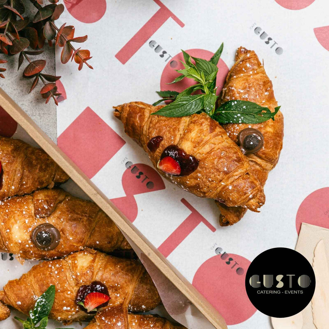 Croissants with berries and mint leaves on a branded tray with 'Gusto' logo.